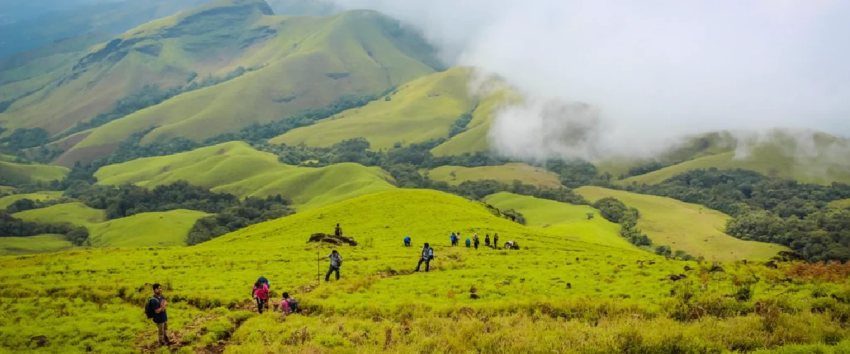 Beautiful view of green hills with clouds and with tourists enjoying the trekking